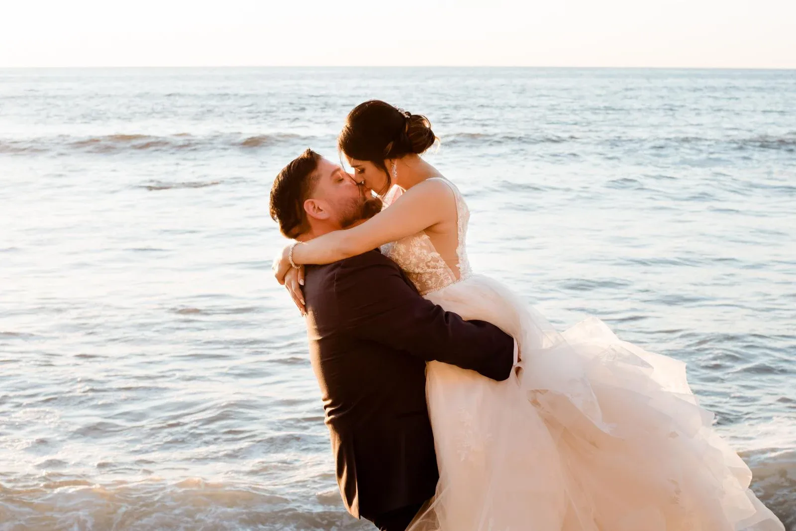 A wedding couple embracing beside waves on a rocky beach