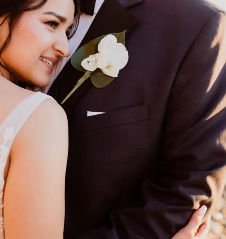 A close crop of a bride leaning against a groom in a dark wedding suit