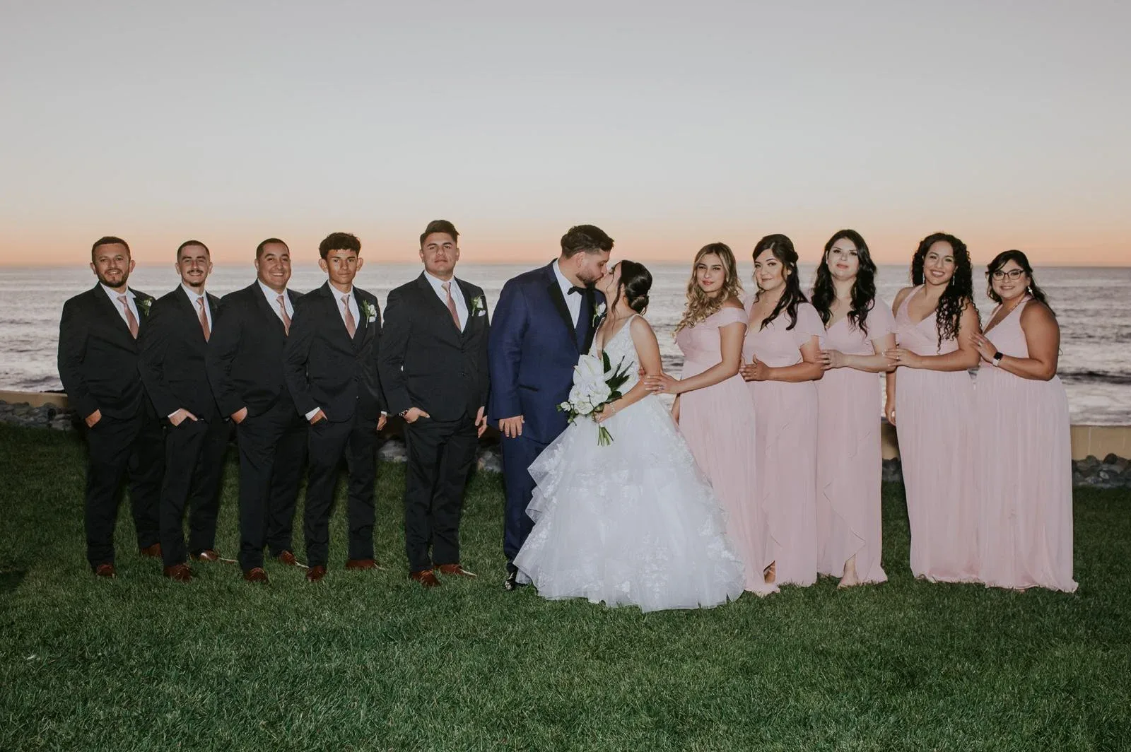 A wedding couple kissing in the middle of their wedding party by the ocean