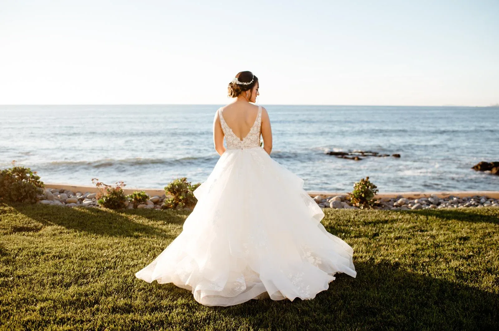 A bride seen from behind in a white gown overlooking the ocean