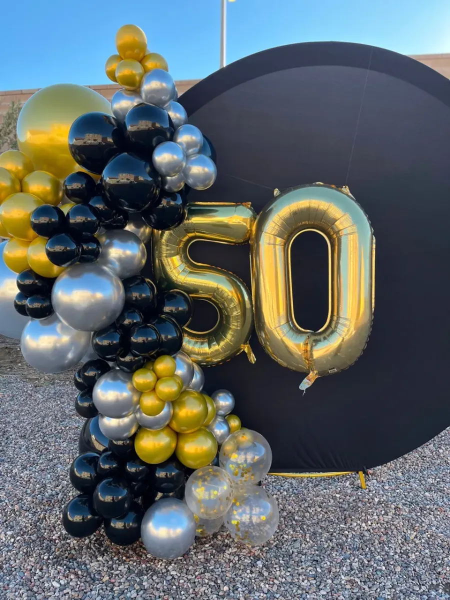 Black, gold, and silver balloons frame a round black backdrop with gold number 50 balloons