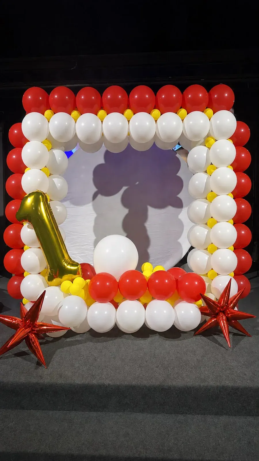 Red, white, and yellow balloons frame a white backdrop with a gold number one balloon
