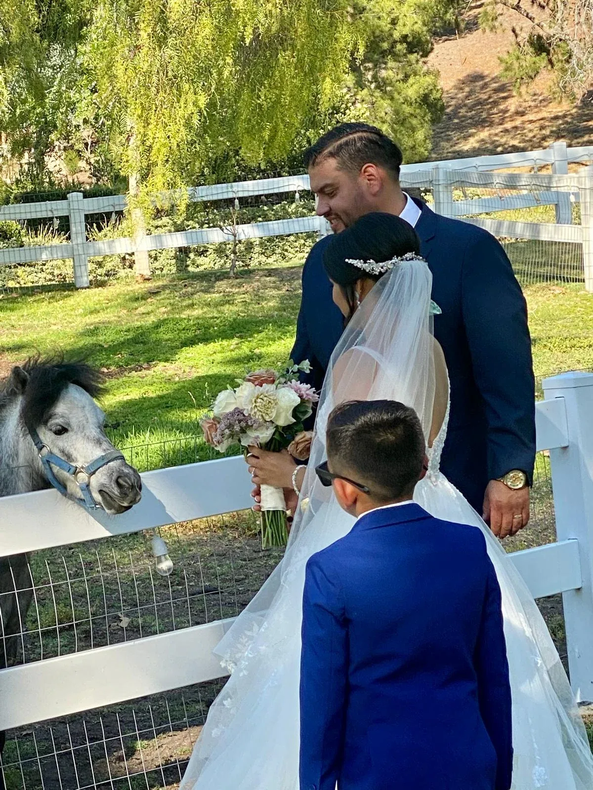 A groom and children beside a white garden fence and flowering greenery