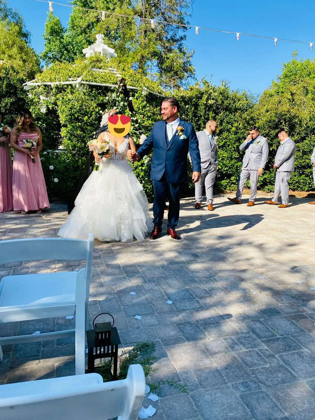 A wedding couple walking down a garden aisle beneath string lights