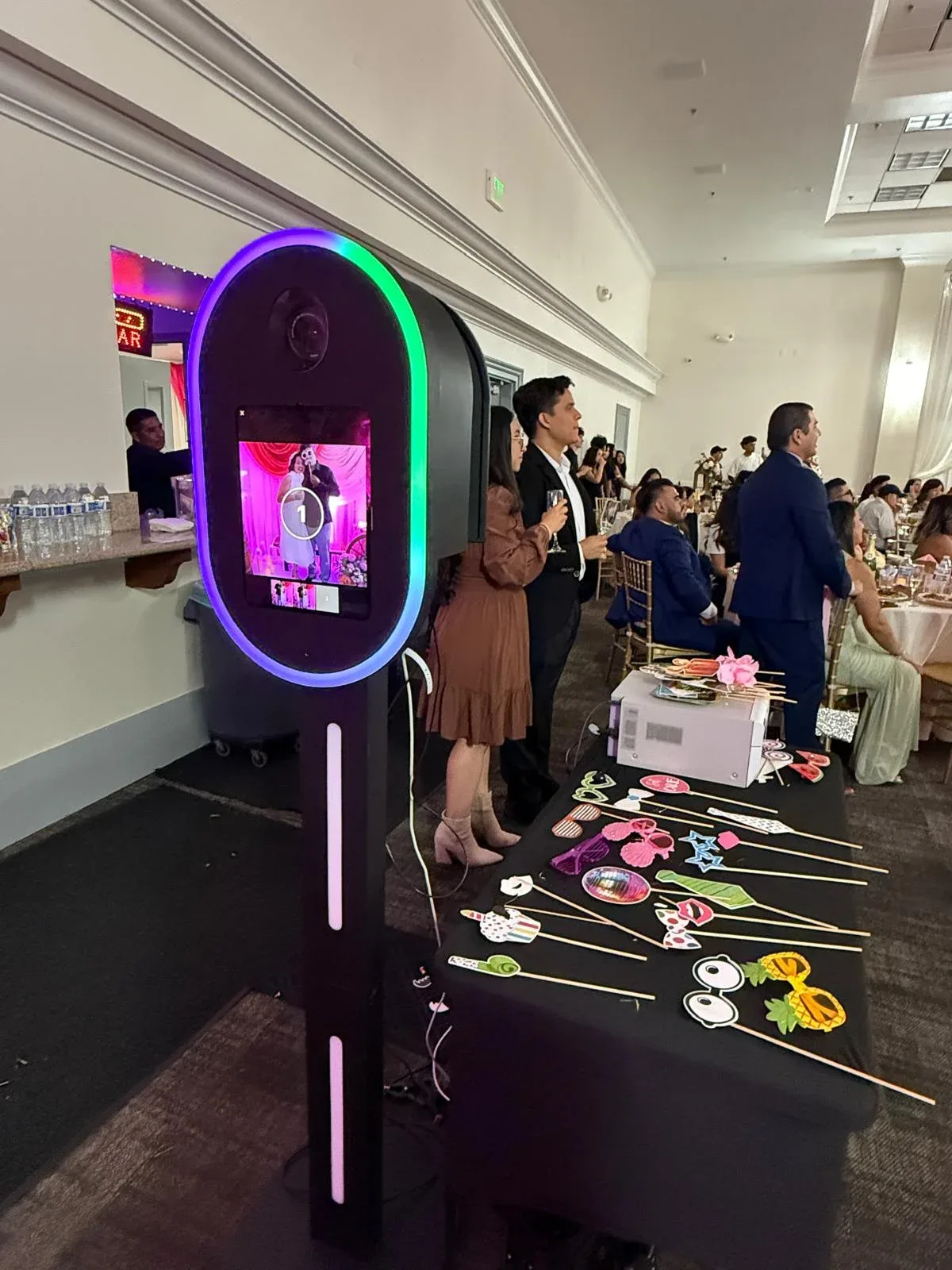 A colorful photo booth and prop table with guests in the reception room