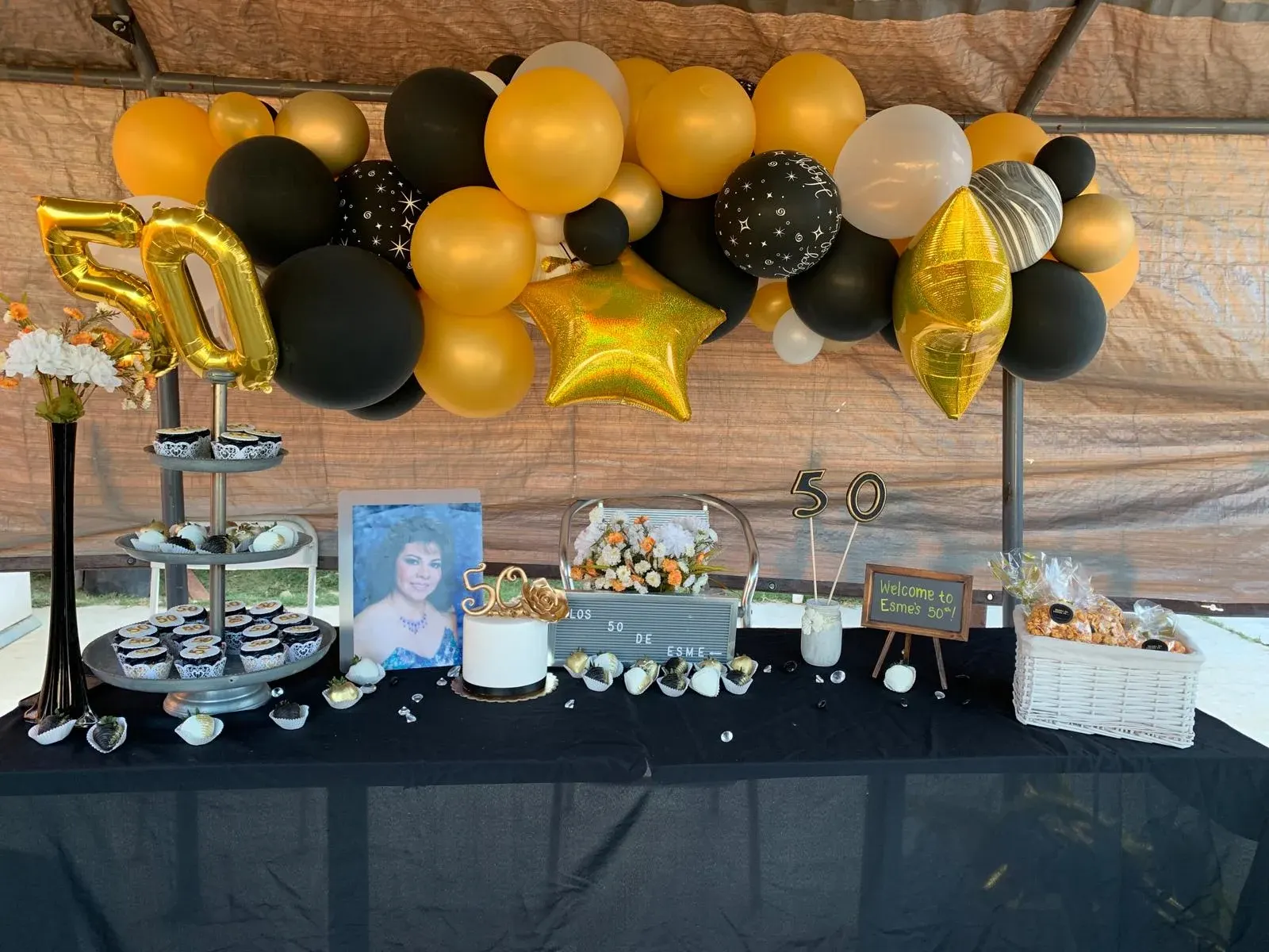 A fiftieth birthday dessert table beneath black, gold, and silver balloons
