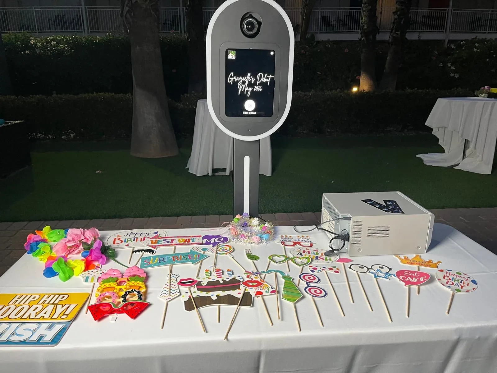 An outdoor photo booth beside a white table of colorful photo props