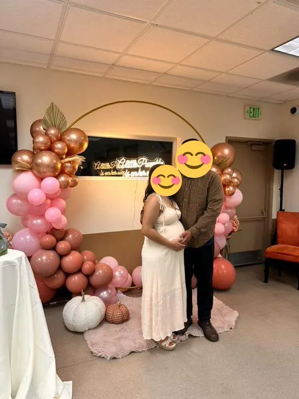 A couple posing beside pink and copper balloons at a baby shower