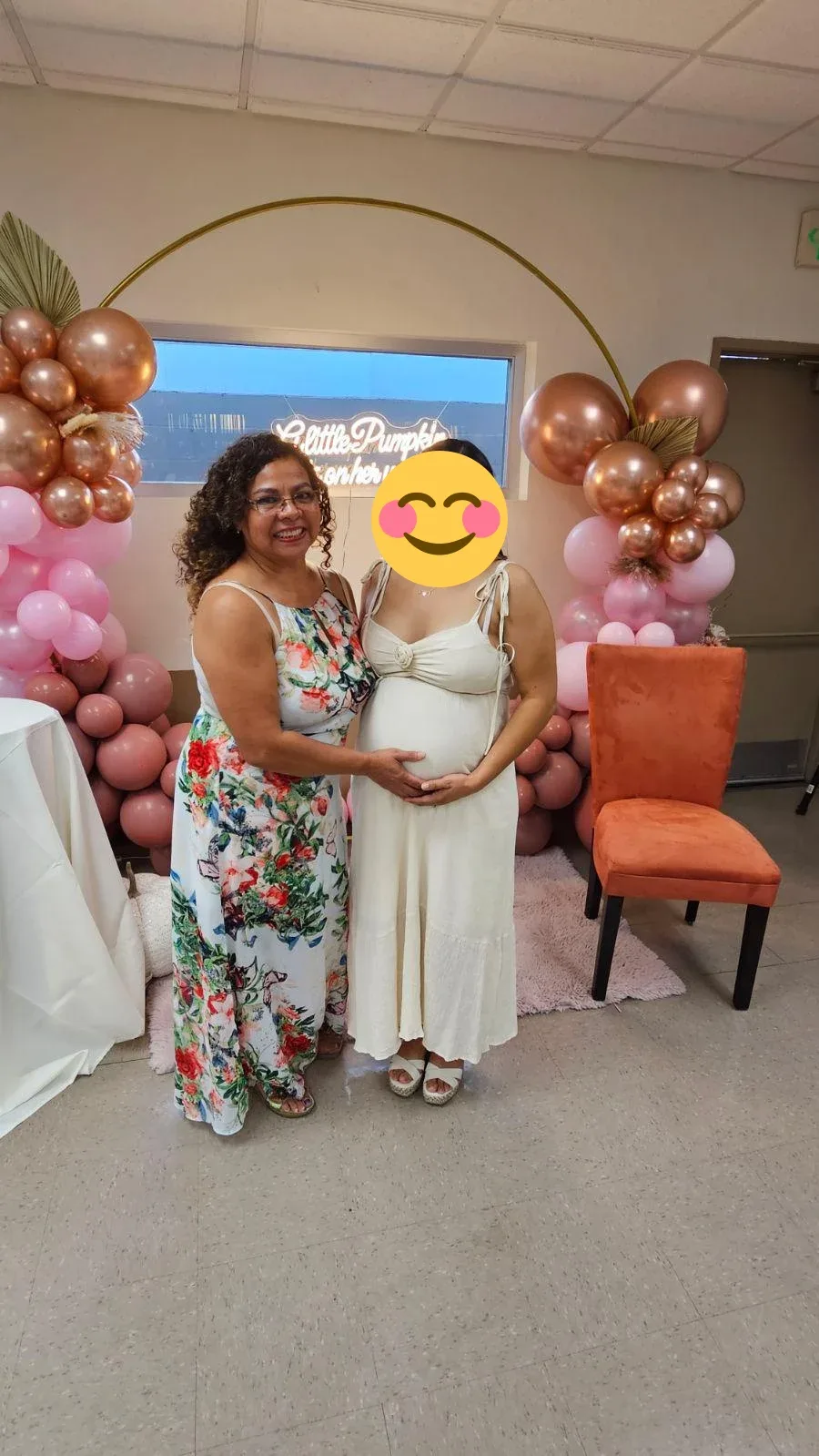 An expectant mother and a relative standing beside pink and copper balloons