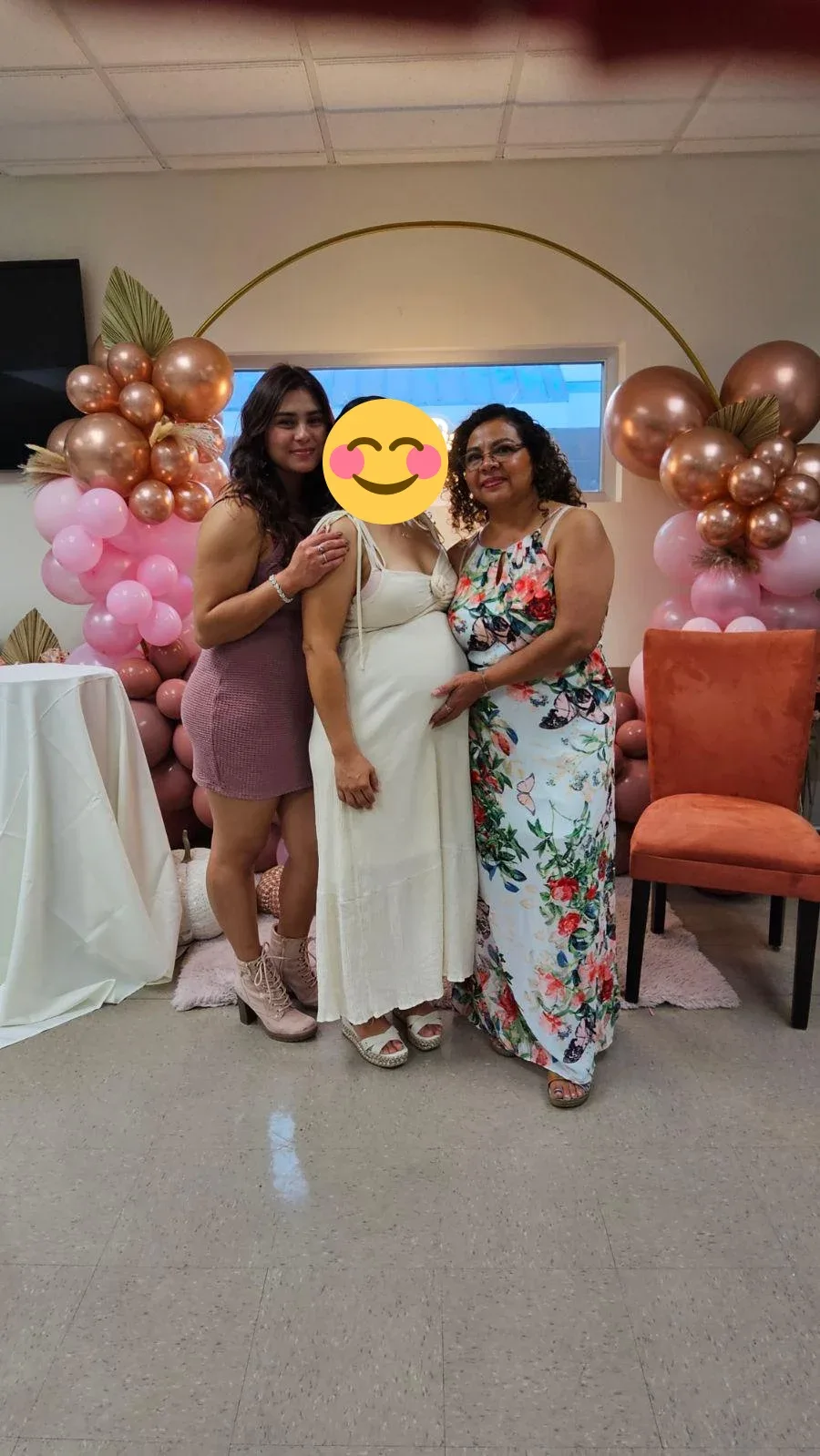 An expectant mother with two relatives beside a pink and copper balloon display