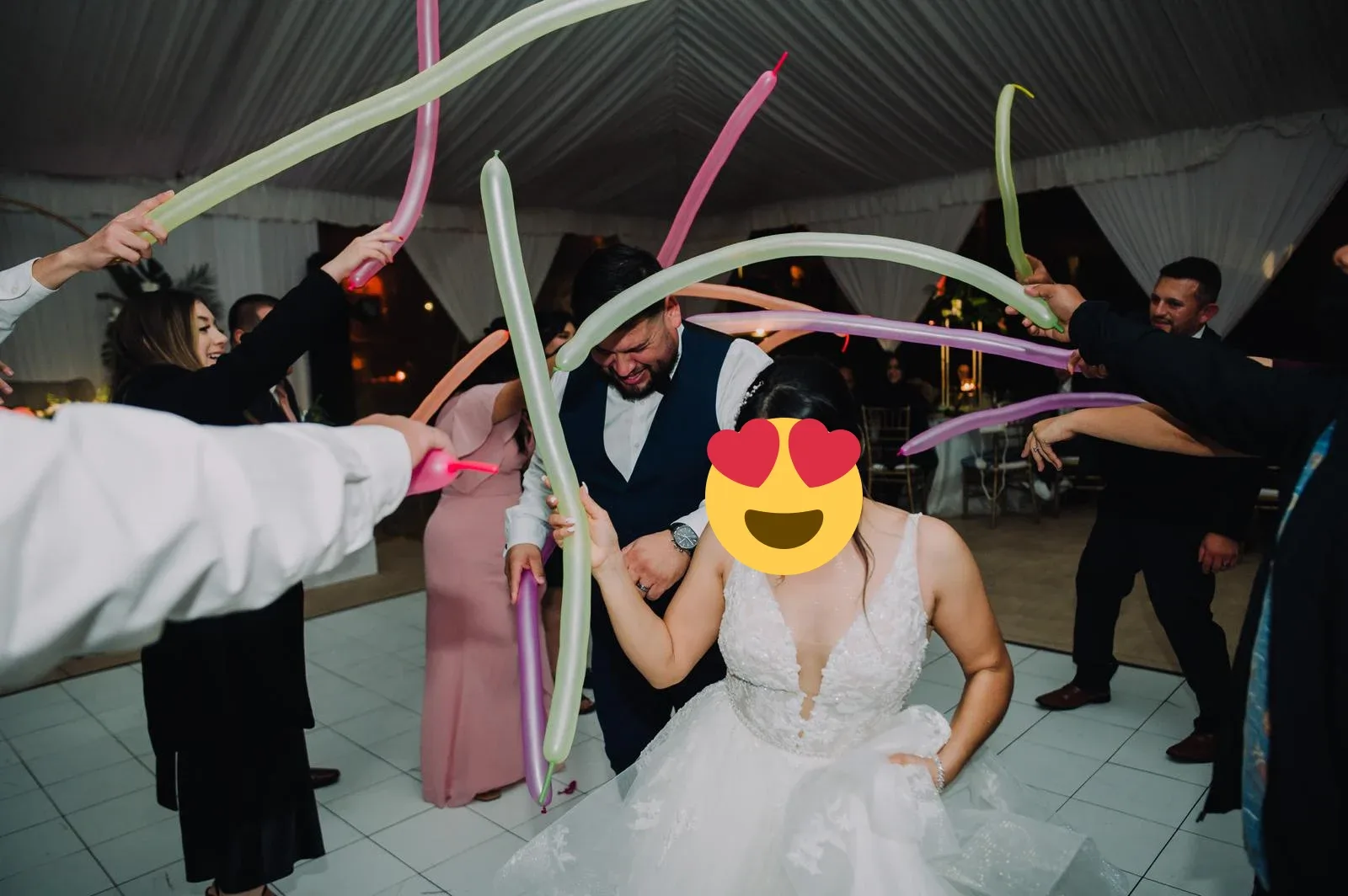 A wedding couple walking beneath colorful balloons held by guests