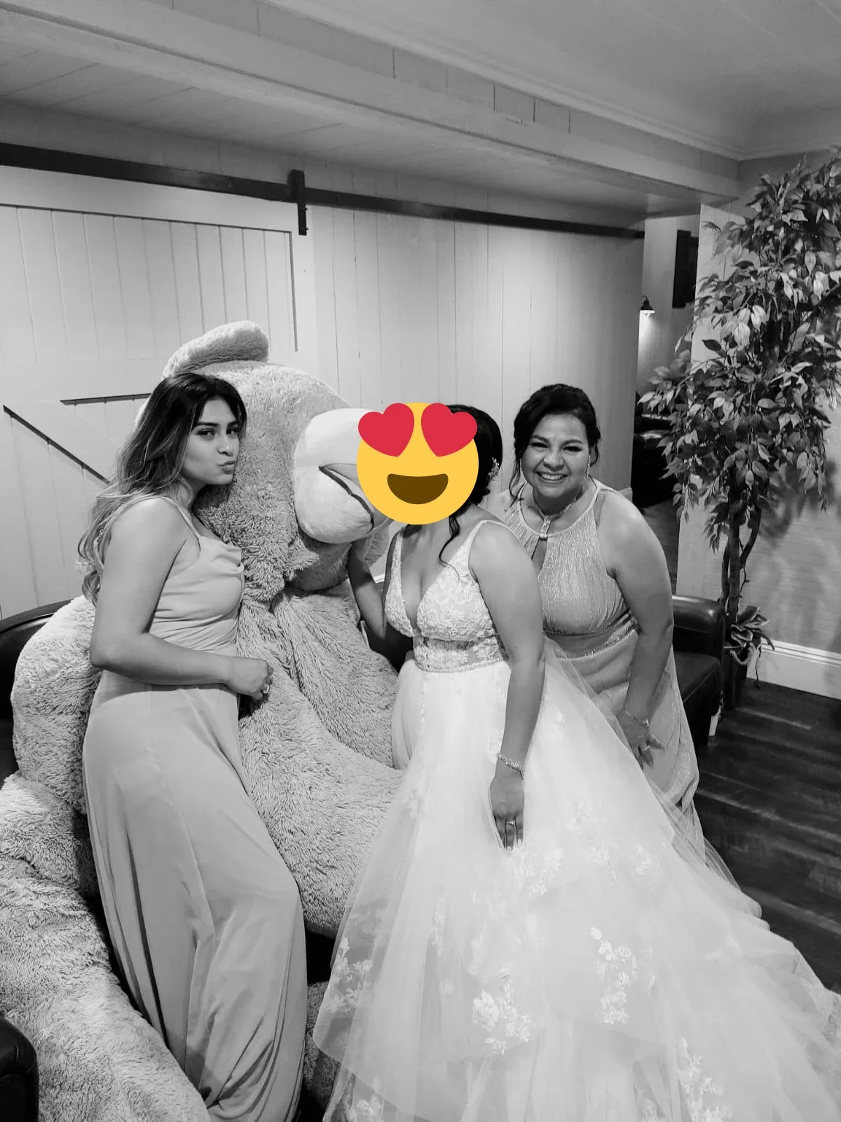 A bride with two companions posing beside a large teddy bear in black and white