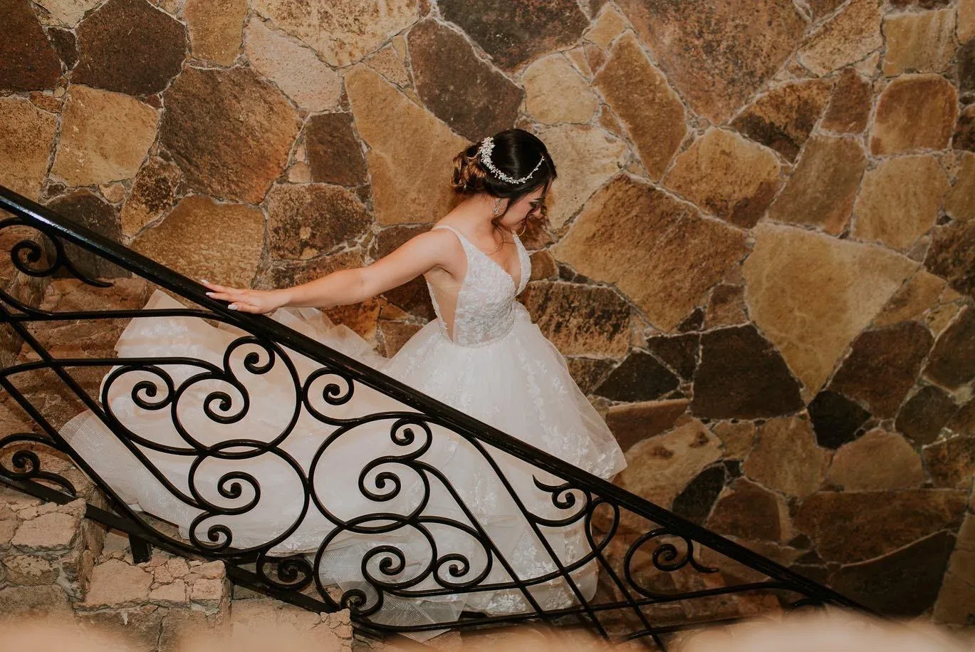 A bride in a white gown on a stone staircase with a curved iron railing