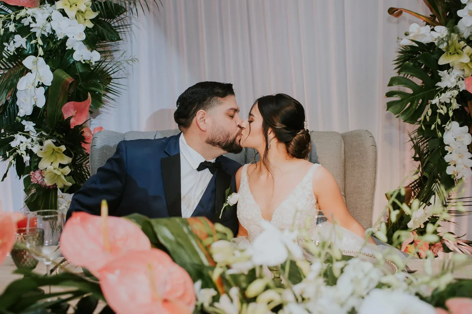 A wedding couple kissing behind flowers at their sweetheart table