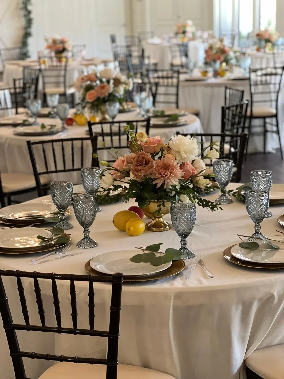 Wedding tables with ivory linens, floral centerpieces, gold chargers, and blue goblets