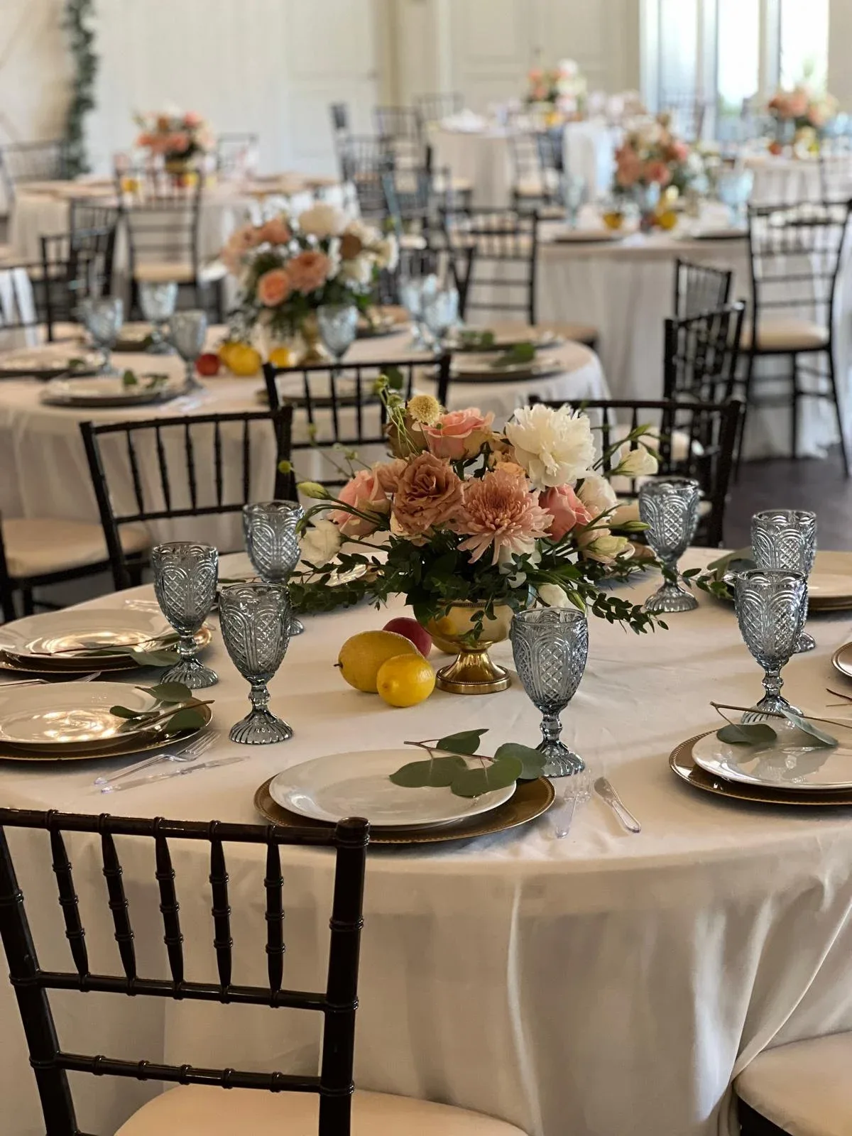 Wedding tables with ivory linens, floral centerpieces, gold chargers, and blue goblets